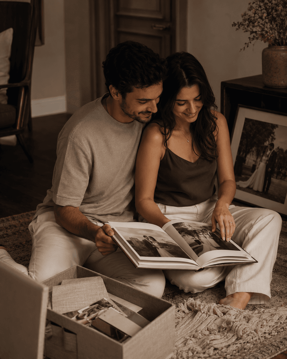 Casal sentado no chão folheando um livro de casamento em uma sala acolhedora.