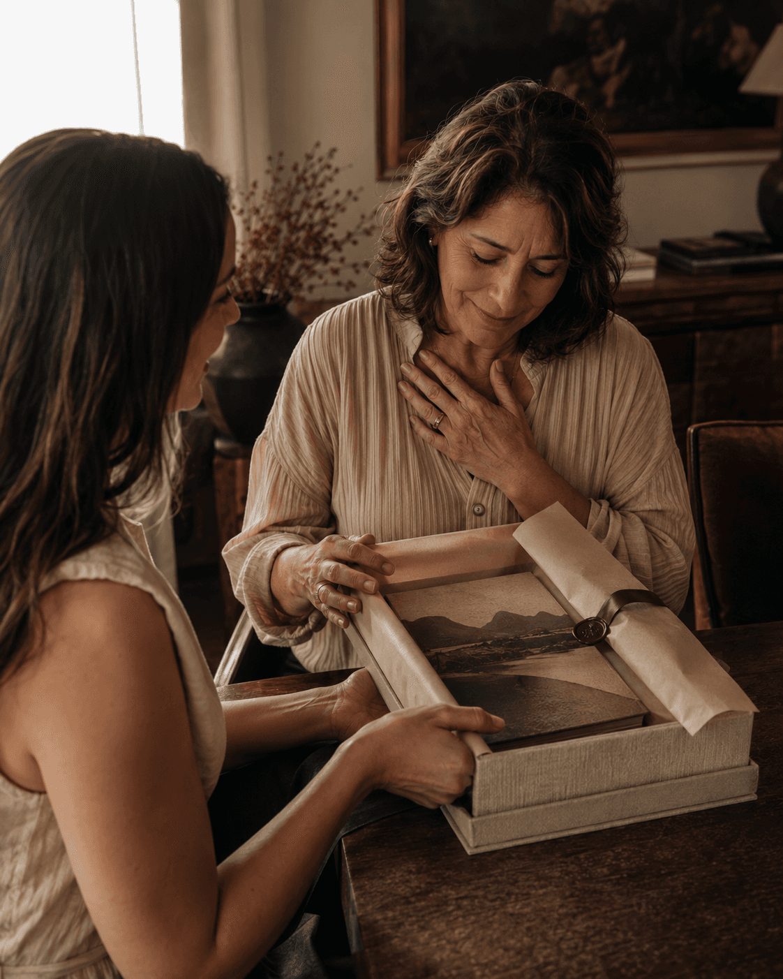 Mulher entrega um livro de memorias a uma mulher emocionada em uma caixa de presente.